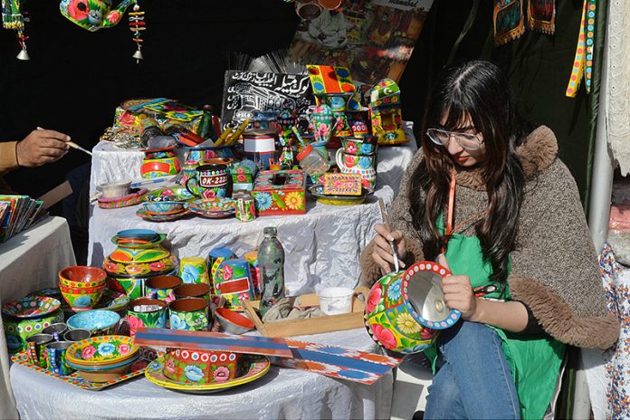 An artist is painting crafts with traditional truck art during ten days “Folk Festival Lok Mela” at Lok Virsa