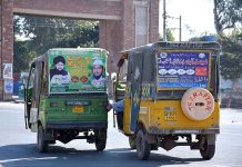 A rickshaw driver pushing another out of order rickshaw heading towards workshop