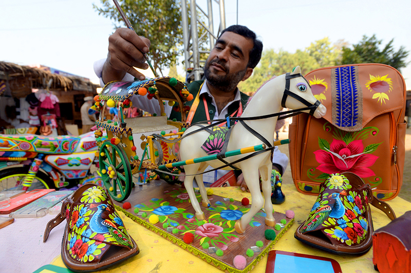 An artisan paints traditional truck art on show pieces during ten days “Folk Festival Lok Mela” at Lok Virsa.