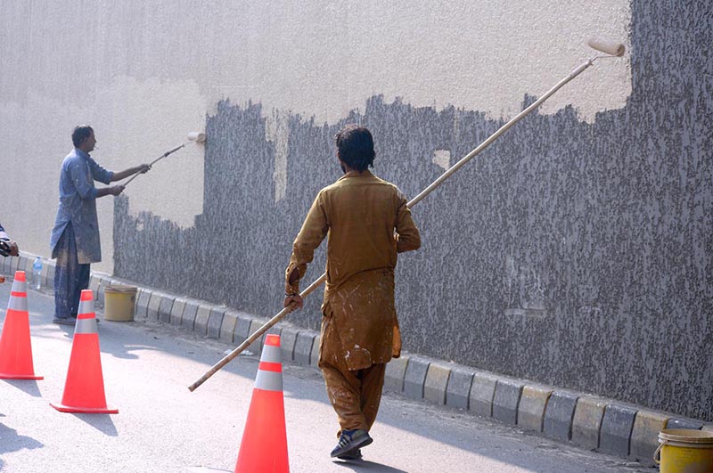 Daily wages laborers painting on wall at roadside