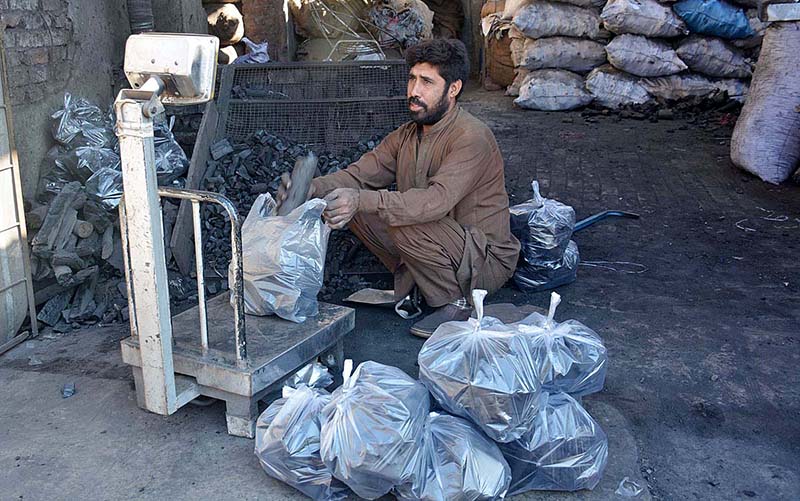 A shopkeeper weighing coal to sell it to consumers as demand increased due to low pressure and shortage of gas during winter season