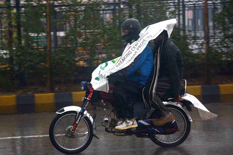 Motorcyclist protecting themselves with banner during rain in the Provincial Capital.