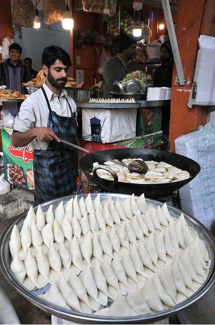 A vendor is preparing samosas for customers at his shop