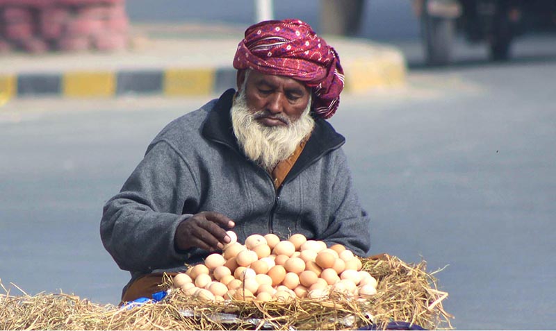 An elderly vendor displaying egg to attract the customer at his roadside setup.