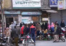 Large number of people in a queue to get groceries outside Utility Store.