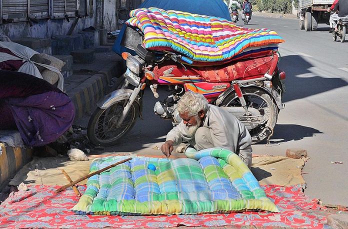 An old man stitching quilt at roadside