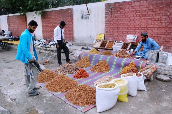 A vendor displaying and selling dry fruits to the customers at his roadside setup.
