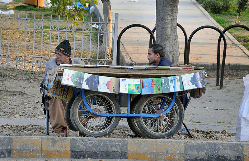 Vendor waiting for customers to sell books displayed on pushcart in Federal Capital