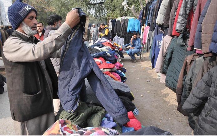 People selecting and purchasing second hand warm clothes from roadside vendor