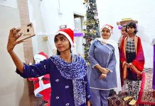 Christian girls taking selfie with decorated Christmas tree at local church in connection with upcoming Christmas