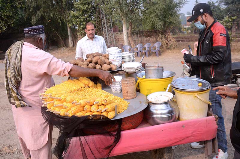 A vendor selling boiled corn cobs and sweet potatoes at his roadside setup.