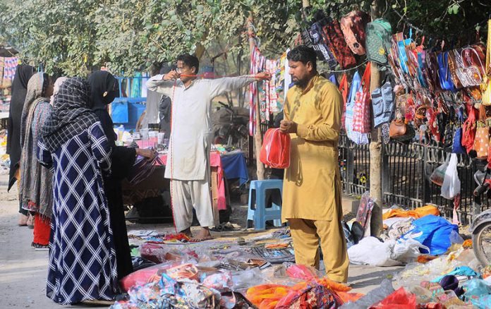 Women customers selecting hand bags from a roadside vendor.