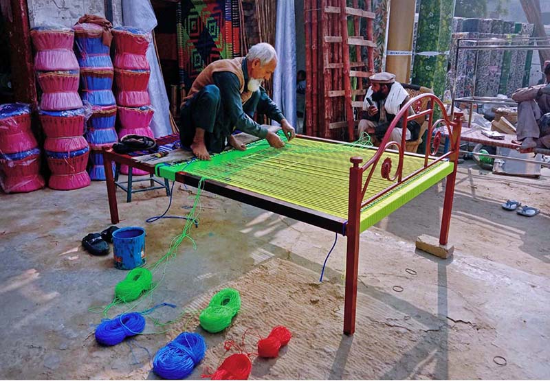 An old man knitting traditional bed (charpai) at his workplace