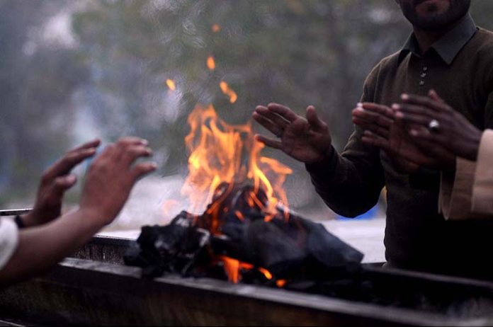 People are getting themselves warm with wood fire during winter season at G-7 Markaz.