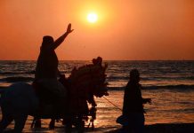 A man riding on a horse waving his hand to say goodbye to the year 2022 sunset at sea view