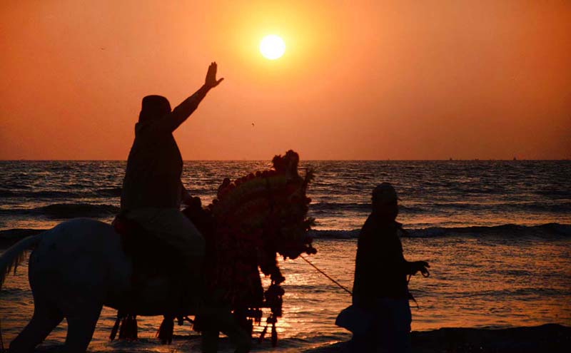 A man riding on a horse waving his hand to say goodbye to the year 2022 sunset at sea view