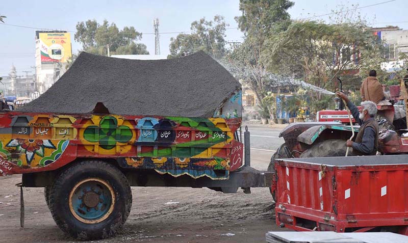A labourer is spraying water on a trolley loaded with sand to avoid sand loss due to jumps and air while travelling
