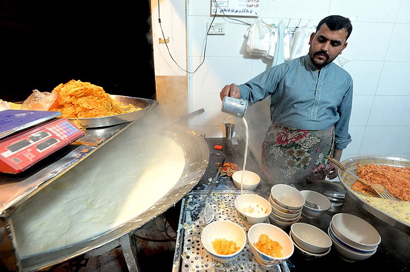 A vendor is preparing a bowl of traditional food item (Dodh Jalebi) during chilled weather for customers at his shop
