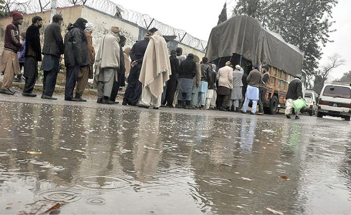 People standing in queue to purchase flour bags on subsidized rates during rain