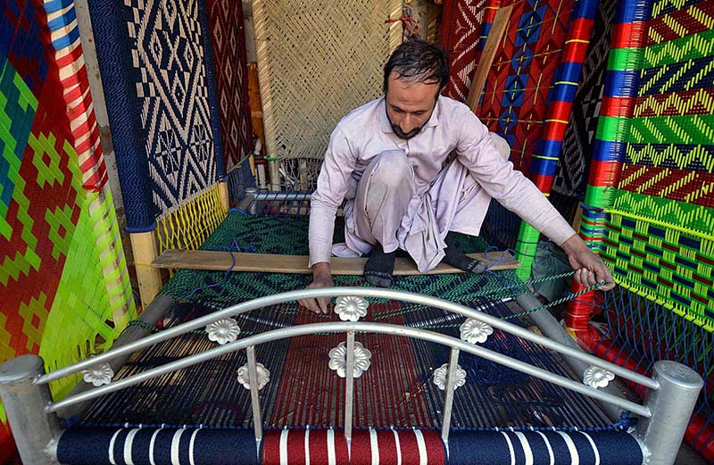 A laborer is knitting a traditional bed (charpai) at his workplace in the Faqirabad Area