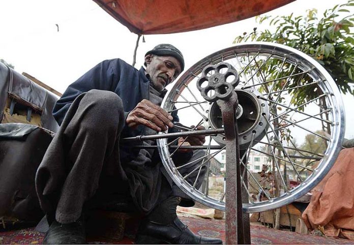 An elderly person busy in alignment of motorcycle tyre rim at Sitara Market in Federal Capital