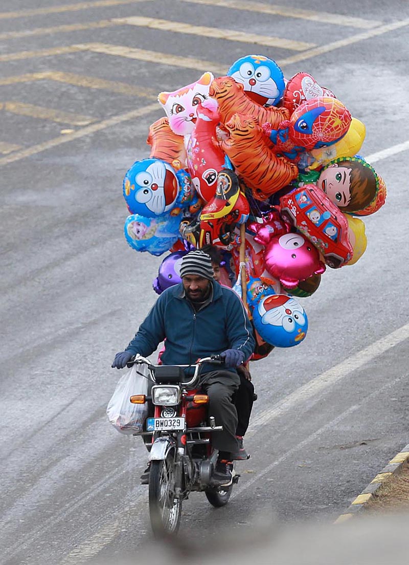 Street vendor on the way riding his bicycle loaded with balloons at Islamabad Expressway