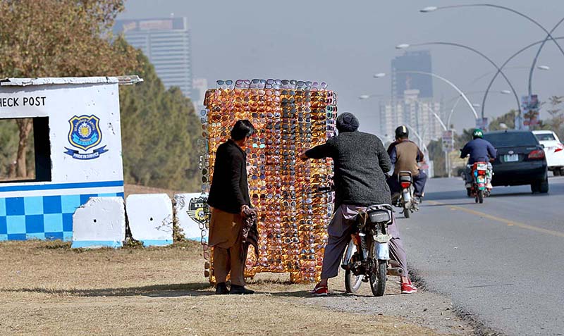 A motorcyclist selecting sunglasses from vendor at roadside in Federal Capital