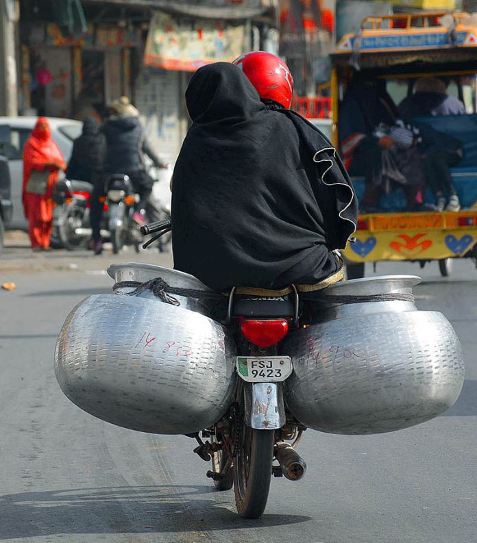 A motorcyclist on the way loaded with two cauldrons