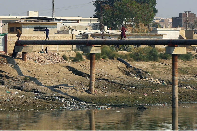 Youngsters crossing the canal by walking on the pipeline at Hala Naka Area