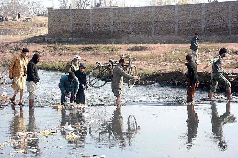 A man is carrying bicycle on his shoulder while crossing a local stream at the backside of Ring Road Cattle Market