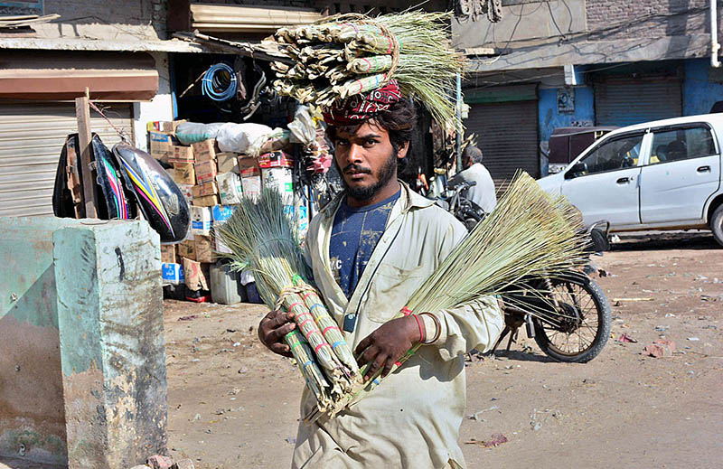 Street vendor carrying and selling brooms at Latifabad