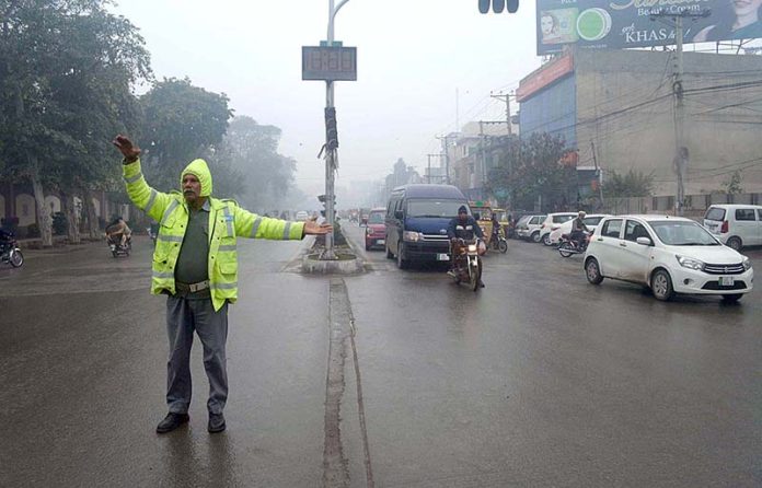 A traffic police official directing traffic at Club Chowk during light rain