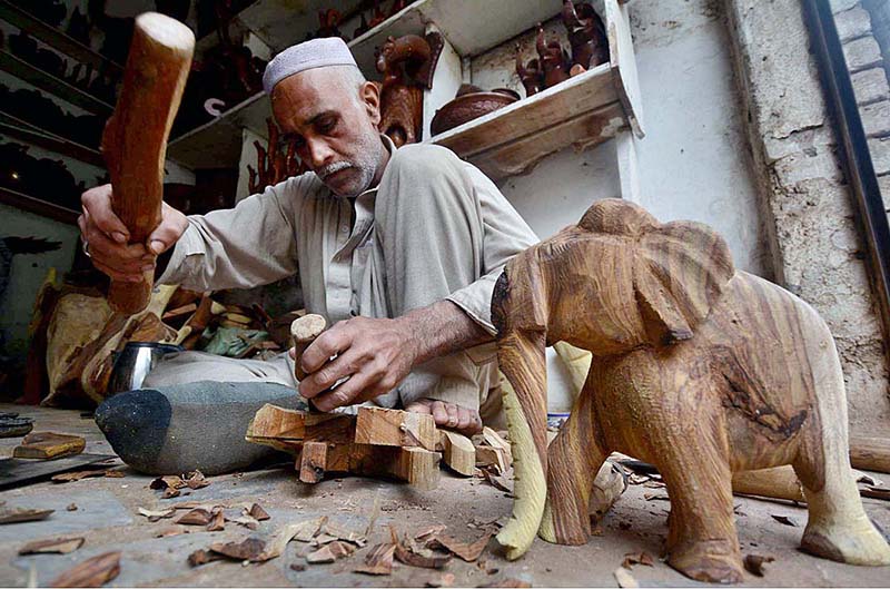 A craftsman making elephants from wood at his workplace near Tehsil Gor Gathri Area