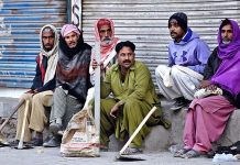 Daily wages Labourers with their tools waiting for costumers while sitting on roadside.