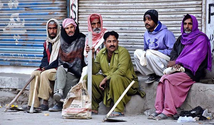 Daily wages Labourers with their tools waiting for costumers while sitting on roadside.