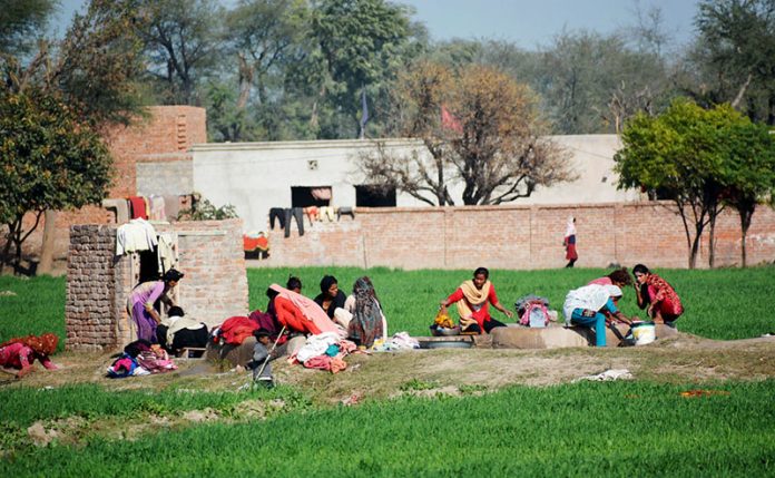 Villager women washing clothes on tube well outside their houses.