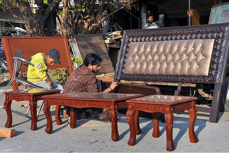 A carpenter polishes for final touch on wooden furniture outside his shop in Sitara market.