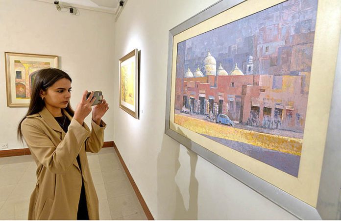 A girl taking photo of a painting during exhibition by Artist Muhammad Javed at Pakistan National Council of the Arts
