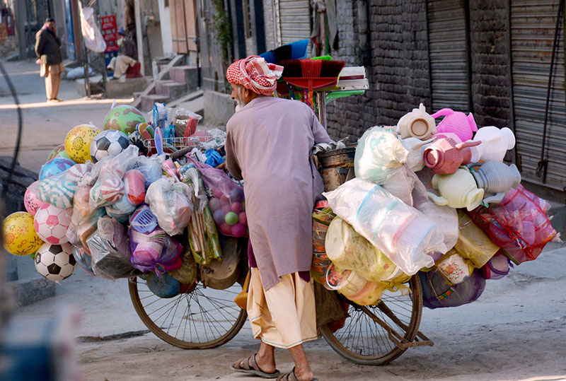 An elderly vendor along with bicycle loaded with household items for selling while shuttling in streets to earn livelihood