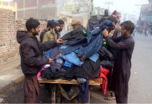 People selecting and purchasing old jackets from roadside vendor.