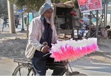 An elderly person selling cotton candy on his bicycle while shuttling on the road