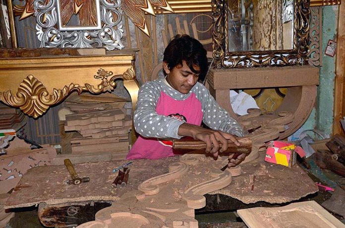 Worker carving design on the wooden sheet at their workplace