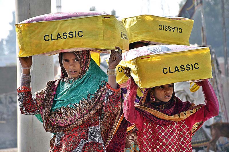 Women street vendors on the way while carrying blankets on their heads for selling at Gul Muhammad Khoso Village Road in the city