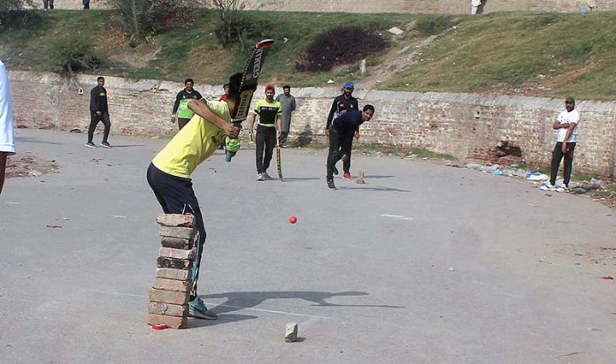 Youngsters playing cricket on the road.