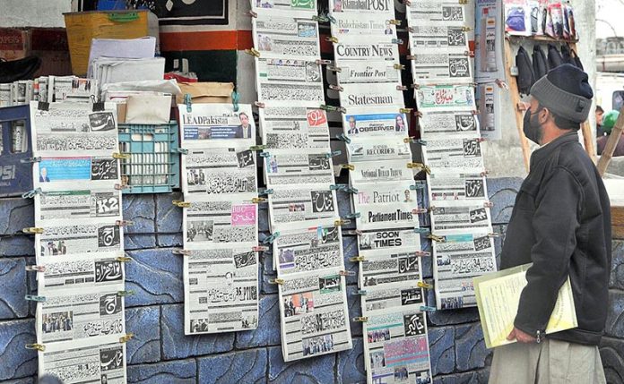 A citizen reads hanging newspapers outside a bookshop to gettingcurrent information at Aabpara market