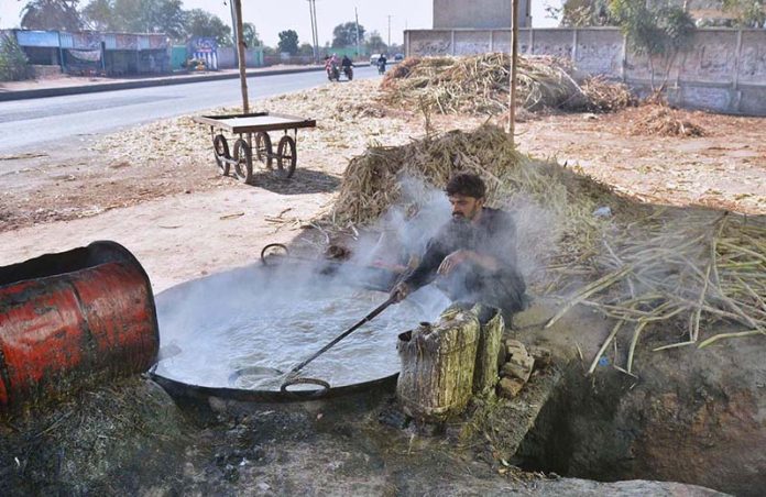 A person boiling sugarcane juice to prepare Jaggery, traditional sweet item Gur near the NLC bypass