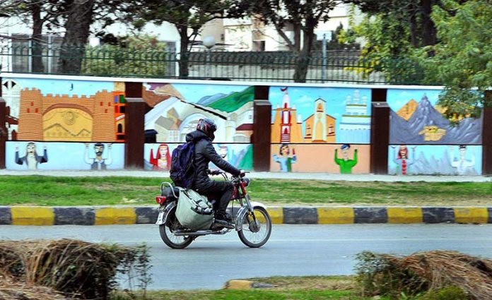 A motorcyclist passing near by a colorful painted wall near a local five star hotel