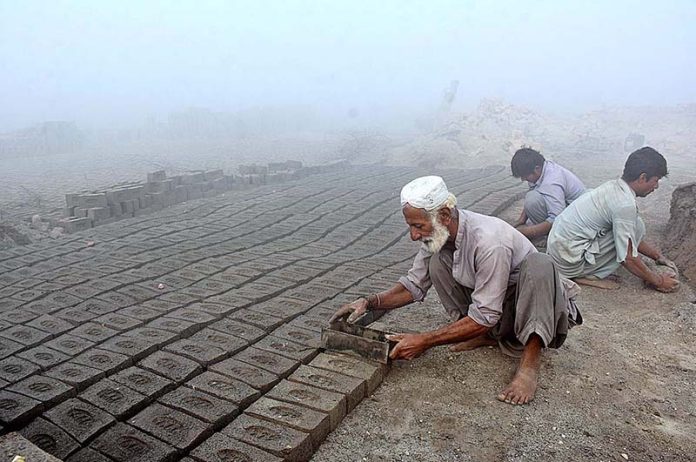Labourers busy in making bricks at a local kiln during thick fog