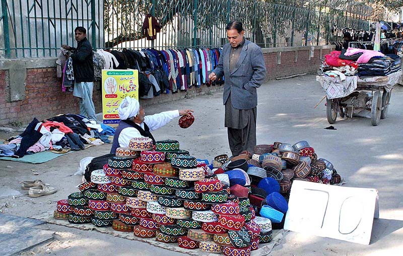 A man is buying Sindhi traditional hat from a roadside stall of a vendor