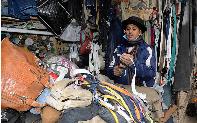 A tailor is repairing zips of jackets and bags at his workplace in Qila Gujjar Singh area